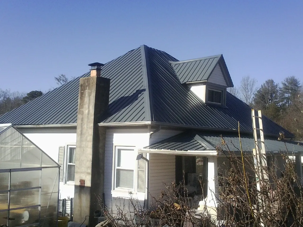 Dark blue standing seam metal roof on a white farmhouse with dormer — Slate & Tile Roof Repair by Roofing Brothers in Eagle